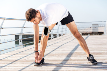 Young sportsman stretching legs during workout on pier