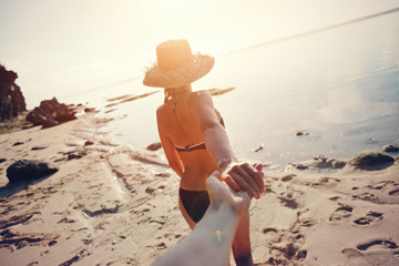 Beautiful woman leading man through the sand beach at sunrise