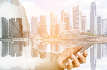 Double exposure of businessman in suit holding smart phone on beautiful city background.