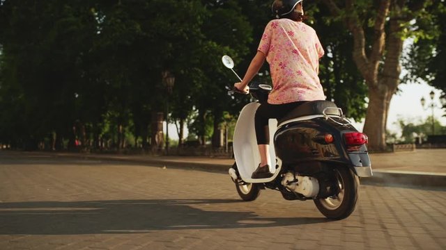 Young beautiful girl riding around city on scooter at sunrise. Slow motion.