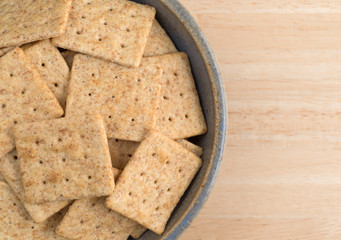 Bowl of organic whole wheat crackers on a wood table top view.