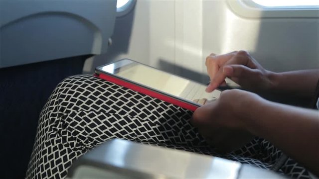 Woman uses tablet computer touchscreen in the plane (close-up)