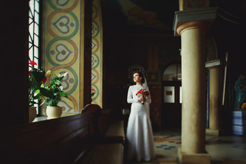 Lonely bride stands behind a bench in church