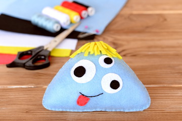 Stitched felt toy, threads kit, scissors, felt sheets on wooden background. Soft funny blue monster. Halloween sewing crafts idea for kids. Children toy project