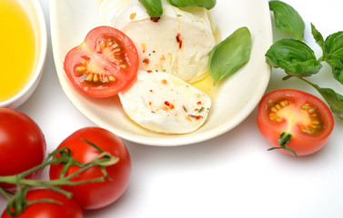 Obraz na płótnie Canvas Delicious cheese mozzarella, tomato and basil leaves in white plate over white background