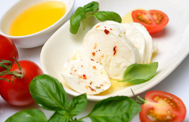 Delicious cheese mozzarella, tomato and basil leaves in white plate over white background