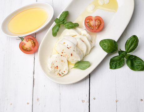 Delicious cheese mozzarella, tomato and basil leaves in white plate over white wooden background