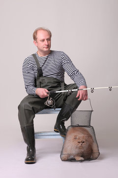 Fisherman in waders sitting on chair, holding a fishing equipment with cat