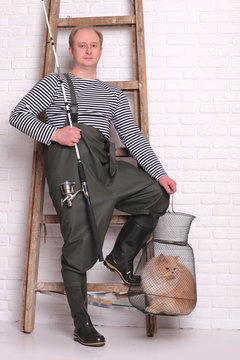 Portrait of fisherman in waders stands near the ladder, holding a fishing equipment