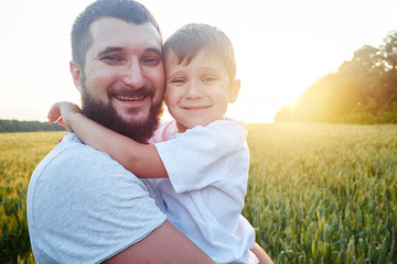 Portrait of smiling dad and son during sunset in the field