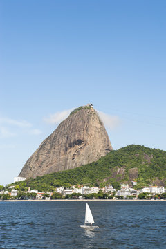 Single sailboat passes classic view of Pao de Acucar Sugarloaf Mountain standing above Botafogo Bay in Rio de Janeiro, Brazil 