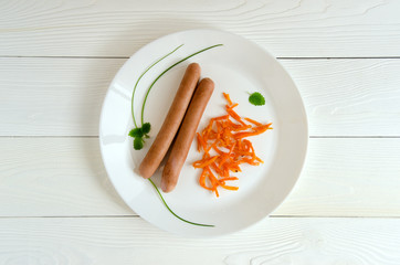 Two sausages white plate carrots top view