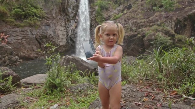Closeup Little Girl in Swimsuit Makes Selfie against Waterfall