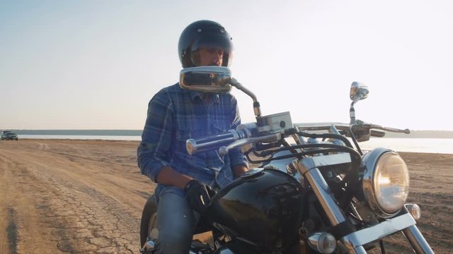 Motorcyclist sitting on his motorbike on the road near the sea during sunset with helmet