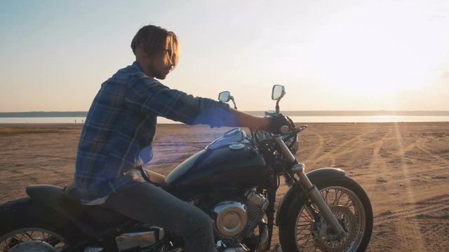 Motorcyclist sitting on his motorbike on the road near the sea during sunset