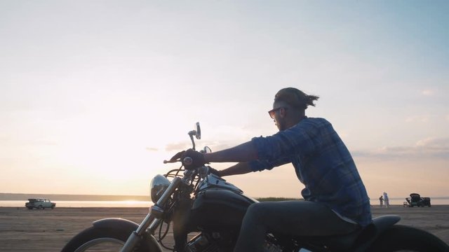 Motorcyclist driving his motorbike on the road during sunset near the water during sunset