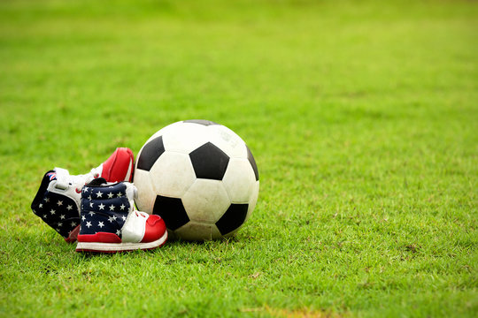 The Close Up Of Kid Shoe And Football In The Field.