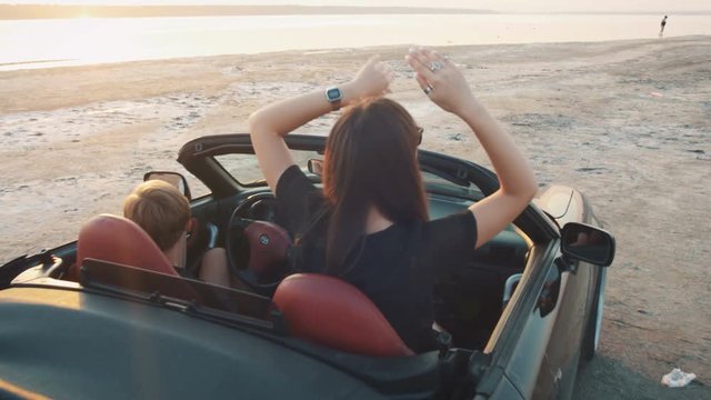 Happy young couple having fun in cabriolet during sunset