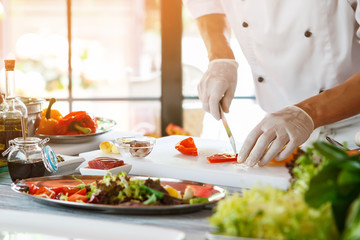 Hand with knife cuts pepper. Pieces of red pepper. Bistro chef preparing lunch. Bell pepper for tasty salad.