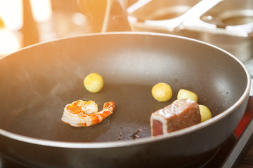 Shrimp on black frying pan. Piece of fish and potatoes. Seafood needs thermal processing. Few minutes and it's ready.