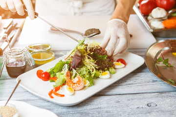 Hands with knife make salad. Salad plate on wooden surface. Salad with frisee and shrimp. Boiled eggs and sliced tomatoes.