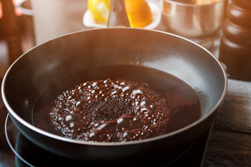 Liquid boiling on frying pan. Black pan with dark liquid. Red wine for sweet sauce. High temperature needed for cooking.