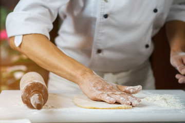 Male hands touching dough. Rolling pin on cooking board. Chef's hand in flour. Precise work of true professional.