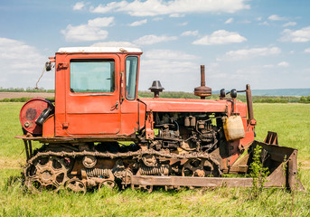 Red old rusty tractor in a field