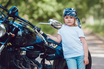 Little girl in a white T-shirt and bandana standing near  motorcycle