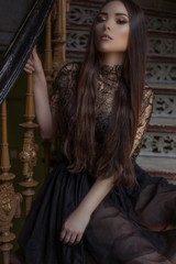 Fototapeta premium Beauty fashion woman with long hair and smokey eyes , sitting on the stair case wearing designer stylish dress 