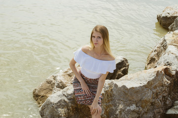 young slender girl is resting on the sea sitting on the rocks