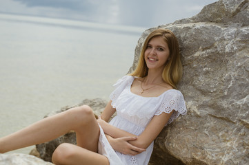 Fototapeta na wymiar young slender girl is resting on the sea sitting on the rocks