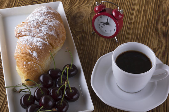 Image of alarm clock, hot coffee and croissant.