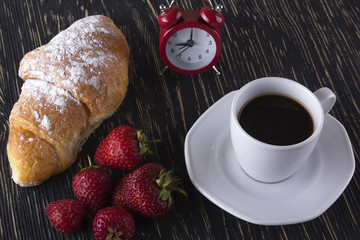 Alarm clock and breakfast with strawberries, coffee , croissant.