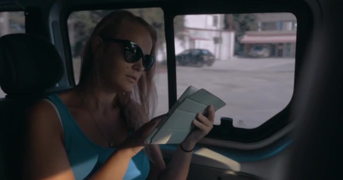 Young woman in sunglasses browsing the internet on tablet computer during car ride in the city