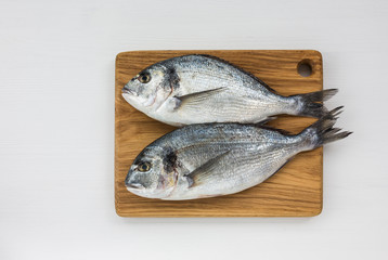 Fresh dorado fish on wooden cutting board on white table. Top view, copy space.