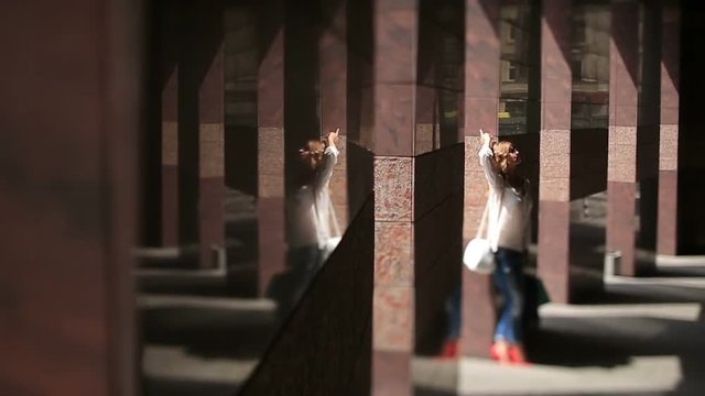 Attractive young woman in sunglasses relaxes in sunlight near marble column of modern city building