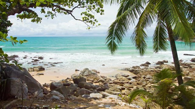 Tourists enjoying a developed section of tropical beach along an otherwise natural and rocky coastline, with palm trees. Video 4k
