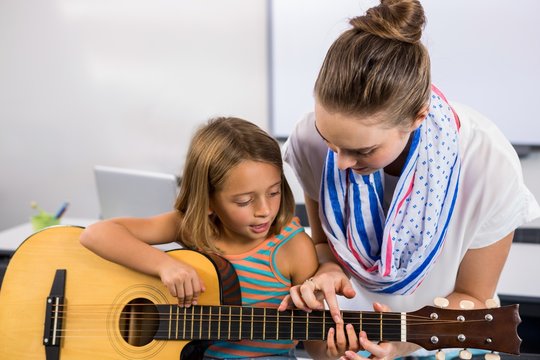 Close-up of teacher assisting girl to play guitar in classroom
