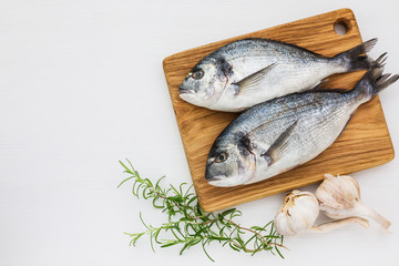 Fresh dorado fish on wooden cutting board with garlic and rosemary on white table. Top view, copy space.