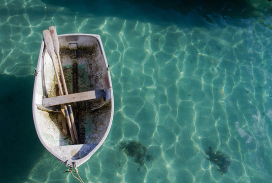 Looking down from above on a small rowing boat with its oars resting inside and tethered to a harbour wall on a calm, green sea.