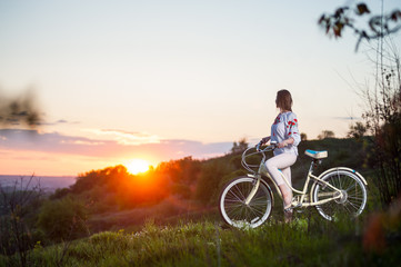 Fototapeta na wymiar Beautiful sunset and sporty woman with bicycle enjoying them. Blurred background