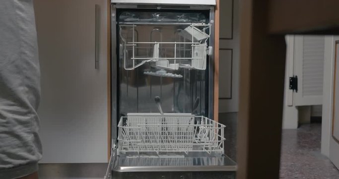 Timelapse of unseen woman putting dirty dishes and cutlery into dishwasher and turning it on