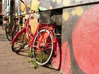 Fahrräder auf dem Gehweg mit Unkraut vor einem bunt bemalten alten Haus mit Graffiti bei...