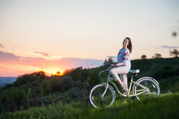 Beautiful sunset and happy girl in Ukrainian embroidery with bike enjoying them. Blurred background