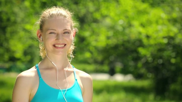 Attractive young woman dressed in white topic smiling at the camera in the park. Portrait of sporty girl.