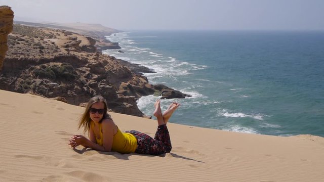 A relaxed young woman lies on sand over breathtaking ocean background view
