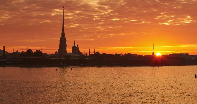 Time-lapse of The Peter and Paul Fortress at sunrise, the quiet waves river Neva, a golden spire with angel on the tower, pink and orange sky, zoom effect