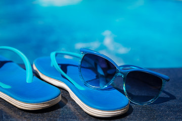 Blue slippers and sun glasses near swimming pool holiday concept