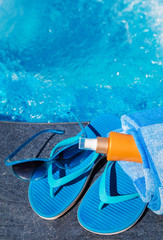 Blue slippers, sunsscreen cream and sun glasses near swimming po